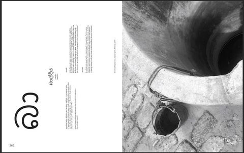 Pages of a book. To our right, a black and white photograph is a view down a well with a bucket tied with a string to our left. The left page has text in English, Sinhala, and Tamil. All are oriented sideways, as if the book opened up instead of out.